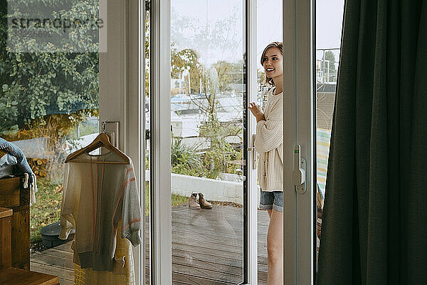 Lächelnde junge Frau  die beim Betreten eines Hauses die Tür öffnet