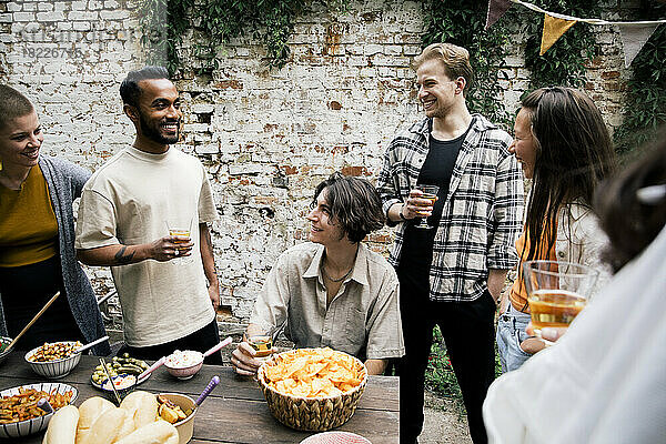 Männliche und weibliche Freunde  die sich bei einer Gartenparty im Hinterhof unterhalten und dabei ein Glas trinken