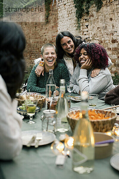 Glückliche weibliche Freunde genießen zusammen am Esstisch während Abendessen Partei im Hinterhof