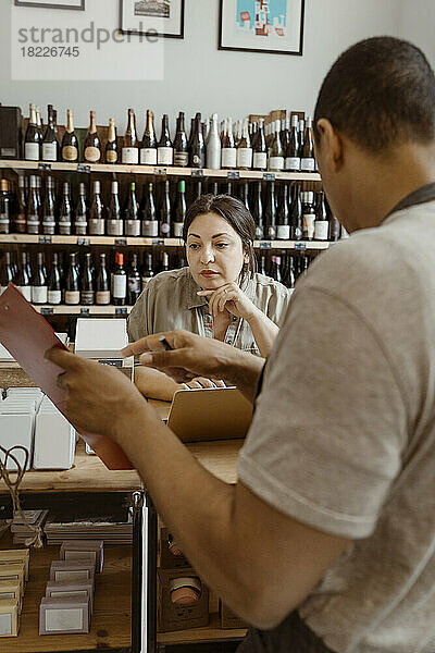 Männlicher Inhaber zeigt einer Kollegin im Weinladen das Inventar