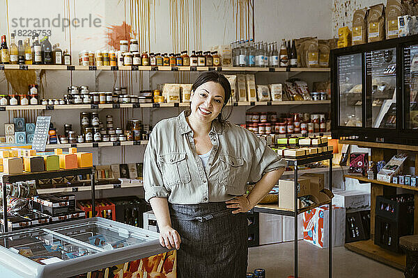 Porträt einer Besitzerin mit Hand auf der Hüfte  die neben einem Eiscreme-Gefrierschrank in einem Geschäft steht