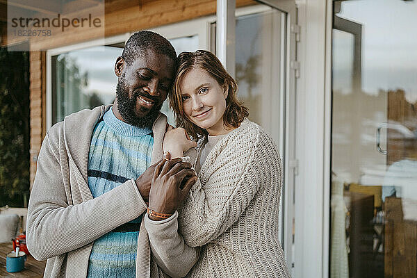 Porträt einer lächelnden jungen Frau  die einen Mann umarmt  während sie auf einer Veranda steht
