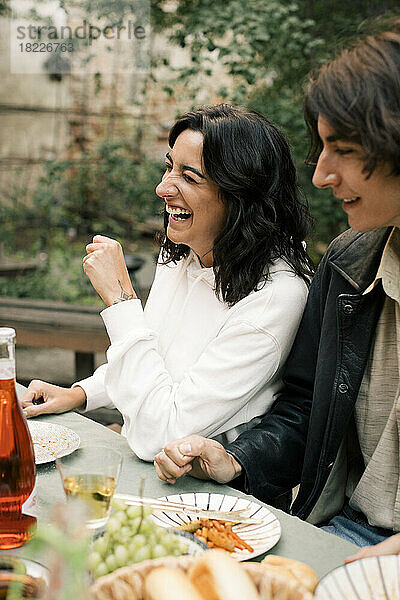 Glückliche Frau lacht  während sie mit einem männlichen Freund bei einer Dinnerparty am Esstisch sitzt