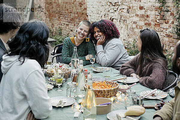 Freunde unterhalten sich mit multirassischen Frauen  die am Esstisch sitzen  während einer Dinnerparty im Hinterhof