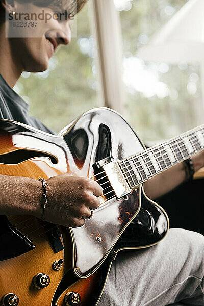 Hand eines lächelnden Mannes  der zu Hause einen Akkord auf der Gitarre spielt