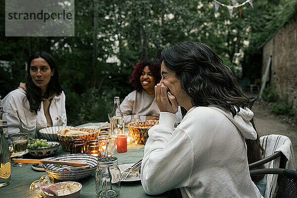 Seitenansicht einer lachenden Frau  die während einer Dinnerparty am Esstisch sitzt