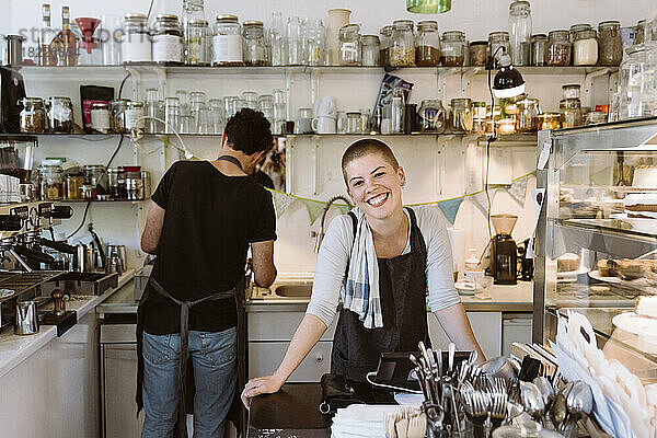 Junge glückliche Besitzerin eines Cafés mit einem männlichen Kollegen  der im Hintergrund arbeitet