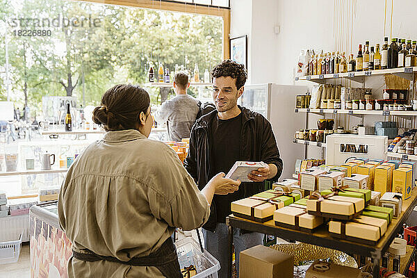 Männlicher Kunde kauft Lebensmittel  während er sich mit der Besitzerin des Ladens unterhält