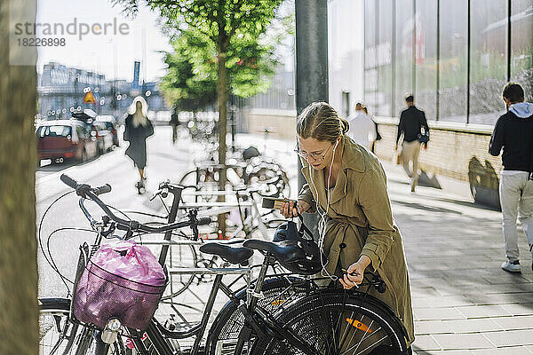 Geschäftsfrau hört Musik  während sie in der Nähe eines Fahrrads an einer Parkstation steht