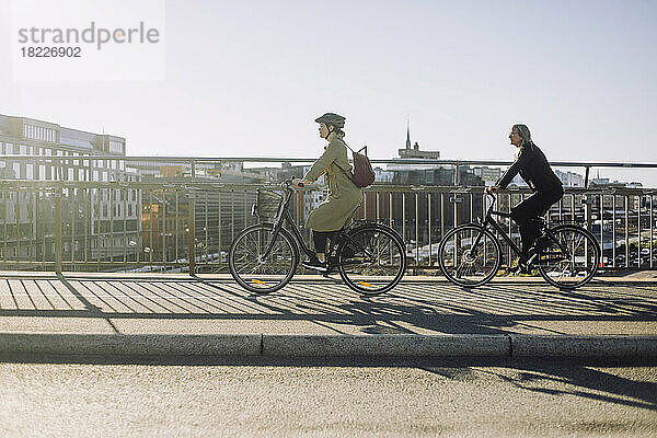 Seitenansicht von weiblichen Geschäftsleuten  die an einem sonnigen Tag mit dem Fahrrad auf der Fahrbahn fahren