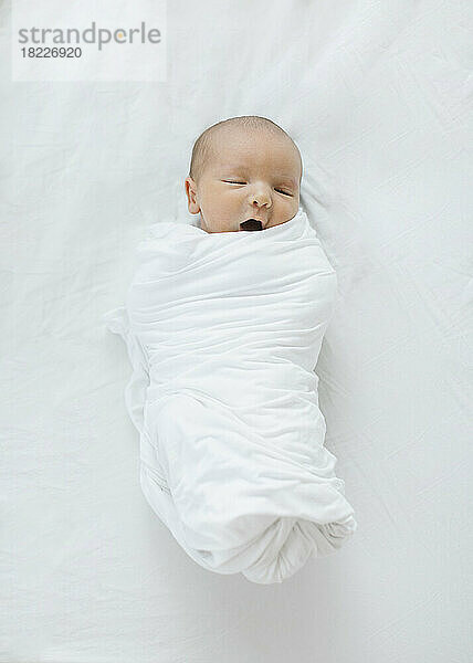Draufsicht auf einen neugeborenen Jungen (0–1 Monat)  der in eine Decke gewickelt ist