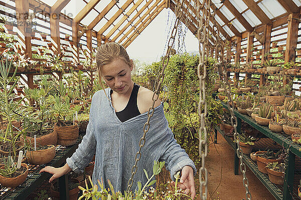 Teenager-Mädchen (16–17) betrachtet Pflanzen im Gewächshaus