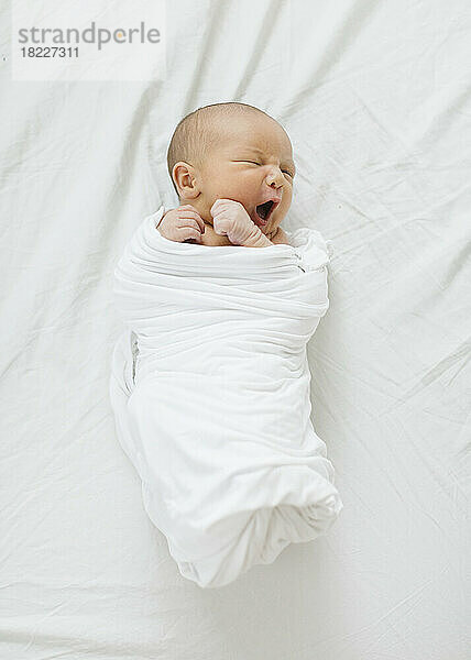 Draufsicht auf einen neugeborenen Jungen (0–1 Monat)  der in eine Decke gewickelt ist