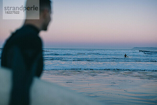 Ein Surfer blickt zur blauen Stunde auf die Welle.