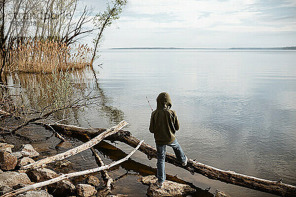Kleiner Junge steht im Frühling am Seeufer und angelt