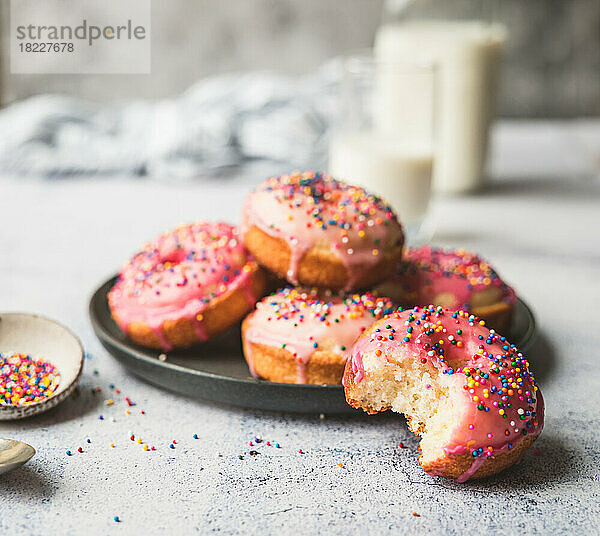 Teller mit Vanillekuchen-Donuts mit rosa Zuckerguss und Streuseln.