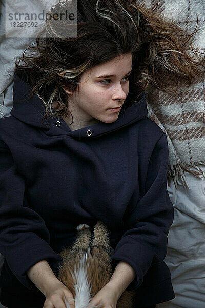 Das Mädchen liegt auf dem Bett und hält eine Katze. Porträt