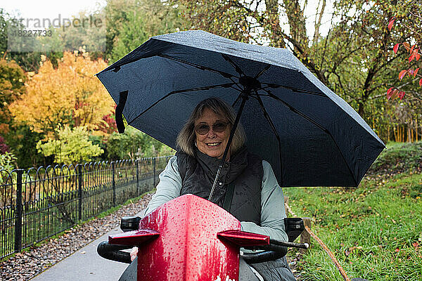 Rentnerin mit Behinderung auf einem Elektroroller draußen im Regen