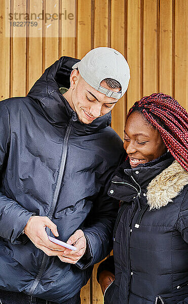 Lächelndes multiethnisches Paar  das auf der Straße auf das Handy schaut.