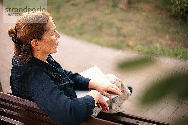 Reife Geschäftsfrau mit Laptop sitzt auf Bank in der Stadt