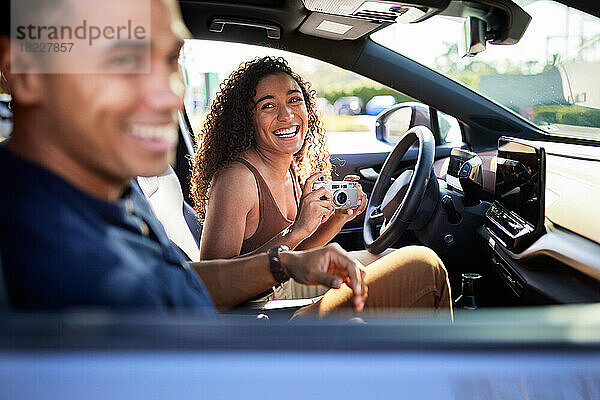 Glückliche Frau mit Kamera blickt während der Autofahrt auf ihren Freund im Auto