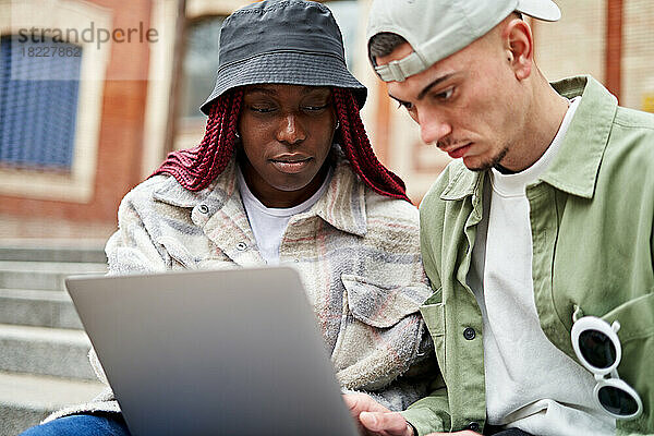 Paar sitzt auf der Treppe an der Universität und arbeitet am Laptop