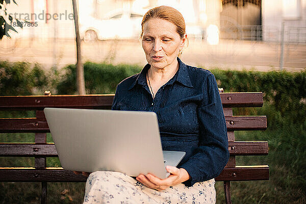 Reife Frau  die einen Laptop-Computer benutzt und einen Videoanruf auf einer Bank führt