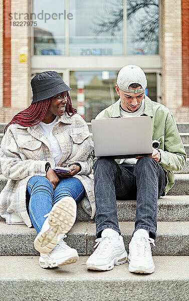 Paar sitzt auf der Treppe an der Universität und arbeitet am Laptop