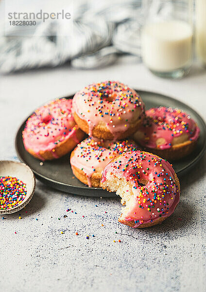 Teller mit leckeren Vanillekuchen-Donuts mit rosa Zuckerguss und Streuseln.