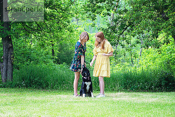 Zwei Teenager-Mädchen vergnügen sich draußen mit einem schwarzen Hund.