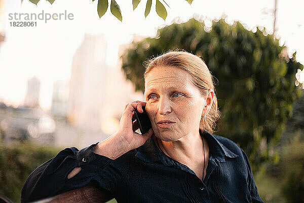 Reife Geschäftsfrau spricht auf einem Smartphone und sitzt auf einer Bank in der Stadt