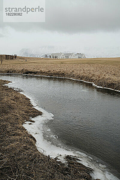 Ruhiger gefrorener Fluss  der durch ein ländliches Feld fließt