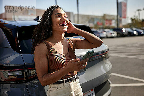Frau mit Smartphone lacht an sonnigem Tag auf Parkplatz