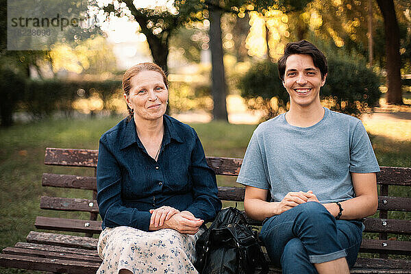 Glückliche reife Mutter und lächelnder erwachsener Sohn sitzen auf der Bank im Park