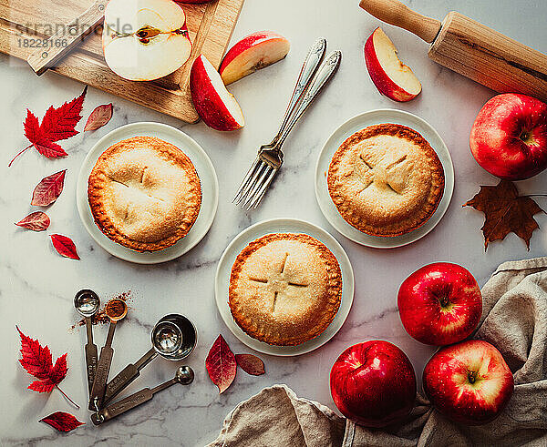 Draufsicht auf Mini-Apfelkuchen und Äpfel auf der weißen Marmortheke.