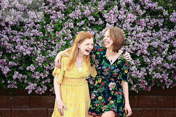 Zwei hübsche Teenager-Mädchen lachen zusammen  umgeben von lila Blüten.