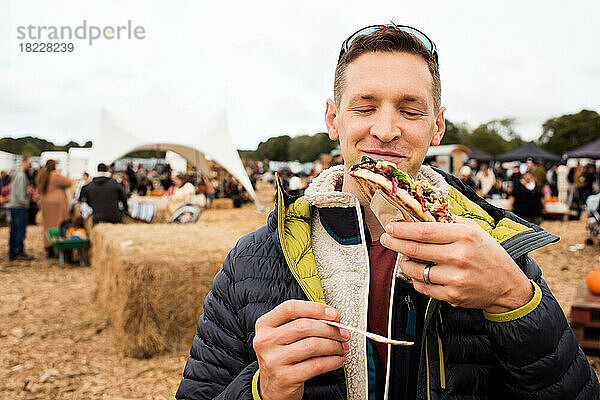 Mann hält Streetfood in der Hand und lächelt auf einem Festival