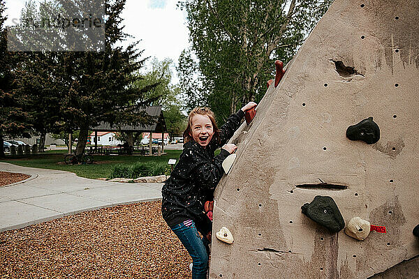 Lächelndes Kind klettert draußen in einem Park auf eine Felswand
