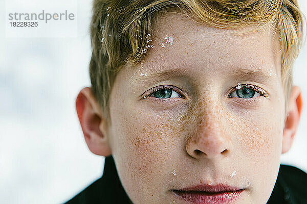 Blauäugiger Junge mit Sommersprossen und Schneeflocken im Gesicht