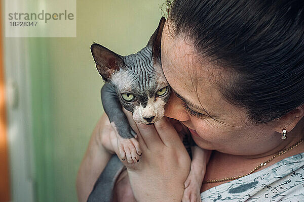 Frau trägt Sphynx-Katze und küsst