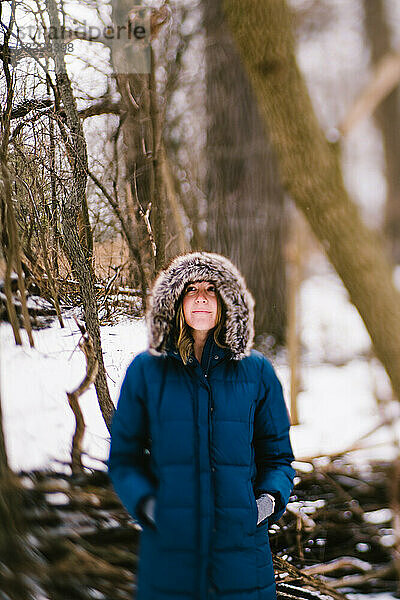 Frau im warmen  mit Pelz gefütterten Kapuzenmantel im verschneiten Wald