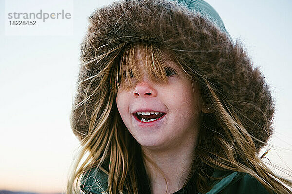 Junges blondes Mädchen im warmen Wintermantel lächelt draußen im Winter