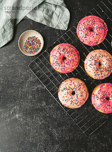 Draufsicht auf Vanillekuchen-Donuts mit rosa Zuckerguss und Streuseln auf dem Gestell.