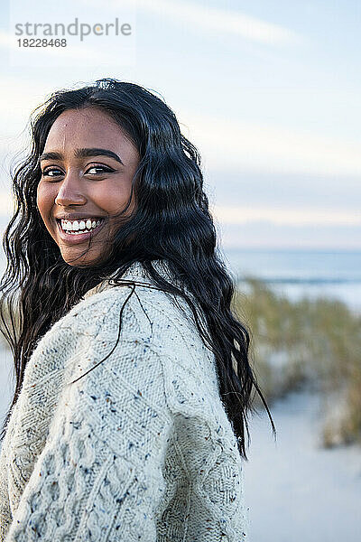 Lächelndes Porträt einer jungen Inderin am Strand  die in die Kamera blickt