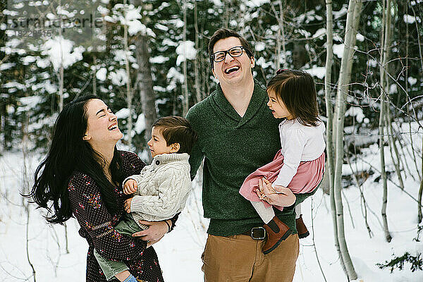 Familie lacht mit zwei kleinen Kleinkindern im verschneiten Wald