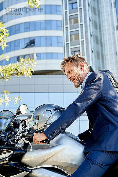 Ein moderner Geschäftsmann im Anzug sitzt draußen auf dem Motorrad