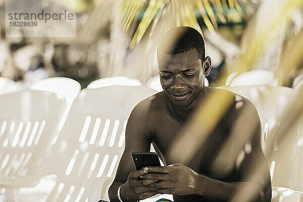 Fröhlicher schwarzer Mann  der sein Smartphone am Strand benutzt