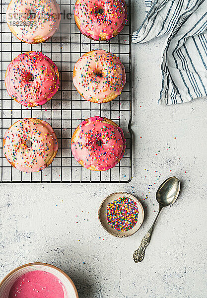 Draufsicht auf Vanillekuchen-Donuts mit rosa Zuckerguss und Streuseln auf dem Gestell.