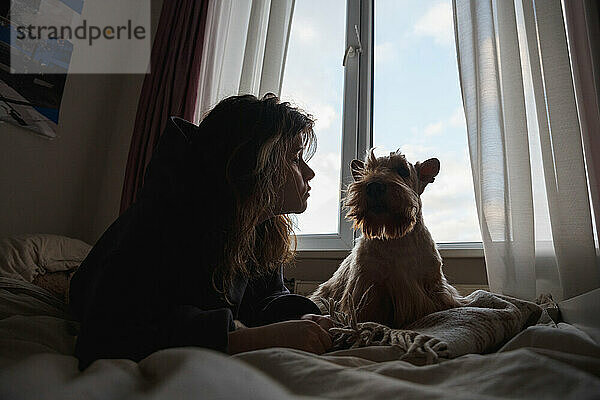 Ein Mädchen und ein lustiger Hund vor dem Fenster.