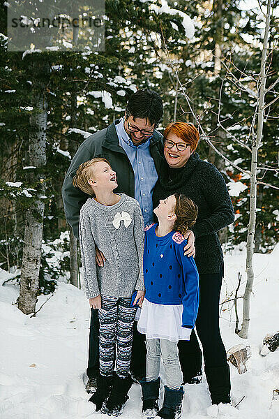 Familie lacht und umarmt sich in Pullovern im verschneiten Wald